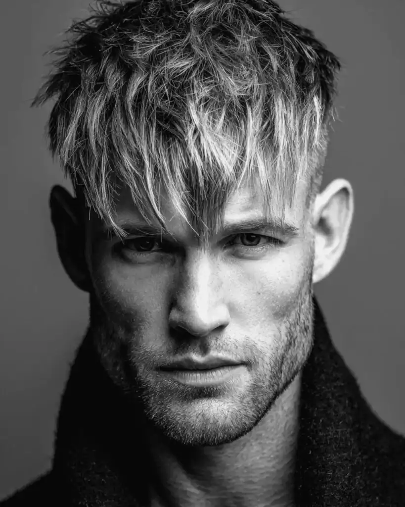 Black and white portrait of a man over 40 with a textured crop hairstyle, featuring high faded sides and heavy, choppy layers styled forward to cover the forehead.