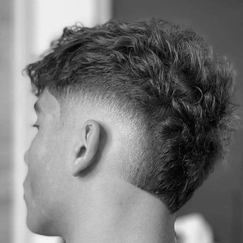 Young male model with a textured mohawk haircut, featuring bold spikes and a sharp fade on the sides, creating a dynamic, edgy look.