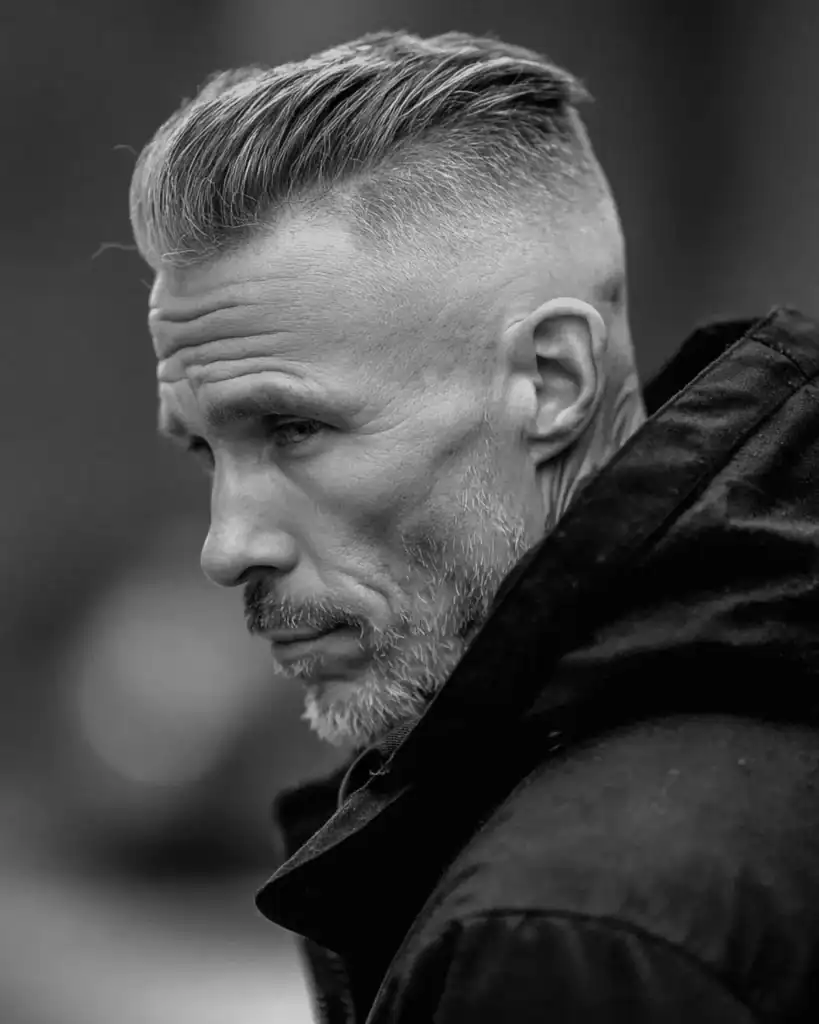 Side profile portrait of a man over 40 with a grey undercut slick back hairstyle, featuring shaved sides and hair styled sleekly back.
