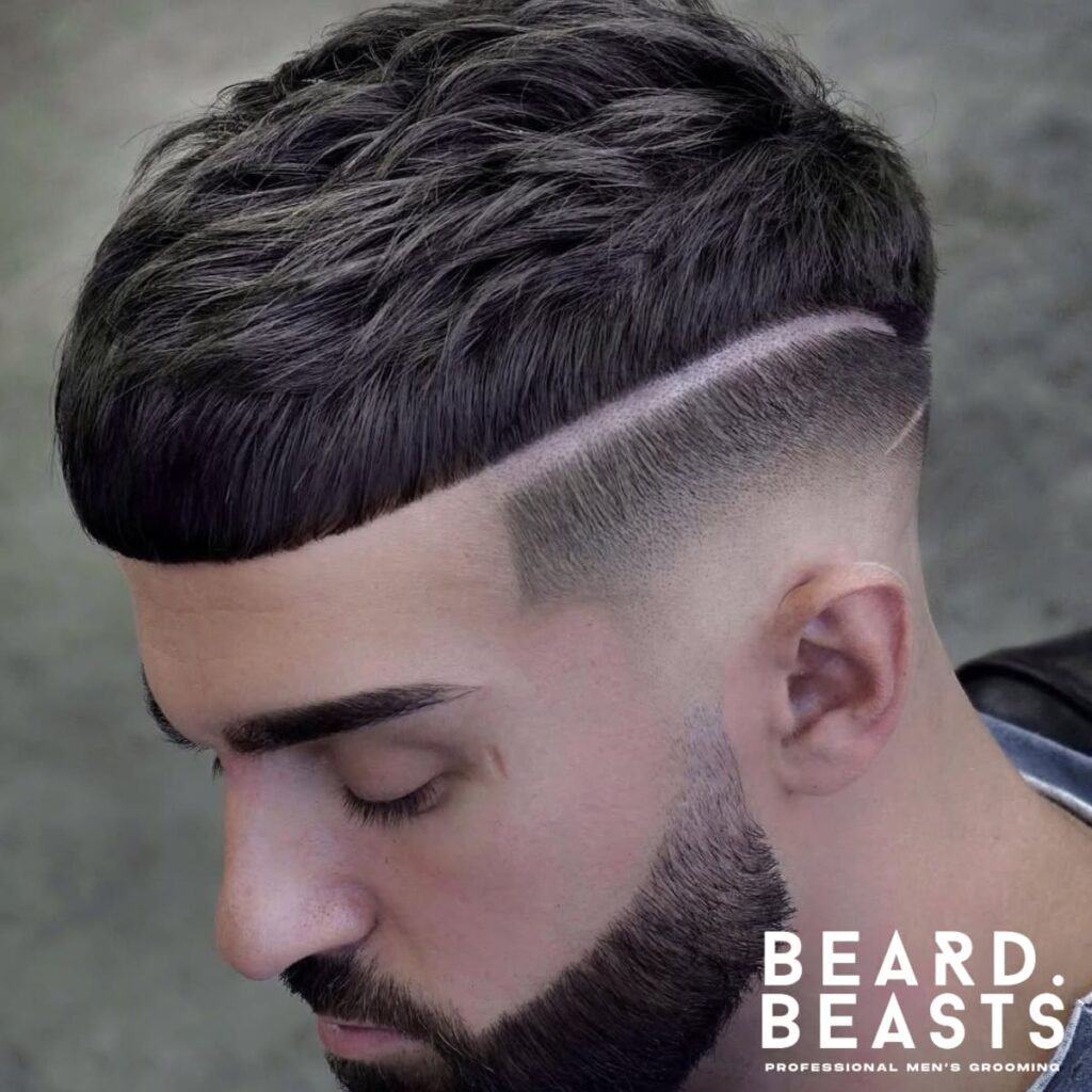 Close-up portrait of a man featuring a sharp, modern haircut with a defined hard part separating the textured top from the cleanly tapered fade on the sides. The hairstyle showcases precision barbering, complemented by neatly groomed eyebrows and a full, styled beard. The man’s thoughtful expression and soft lighting emphasize the details of the haircut and beard. A striking example of a polished and structured men’s hairstyle.