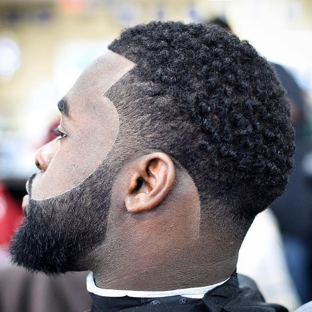 Black man with a short curly afro and sharp line-up, showcasing defined texture and a clean, rounded silhouette with a fade.