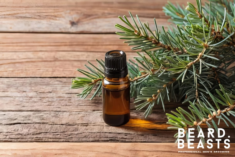 A small amber bottle of cedarwood essential oil placed on a wooden surface, surrounded by fresh cedarwood branches, highlighting its natural use in beard growth and grooming routines.