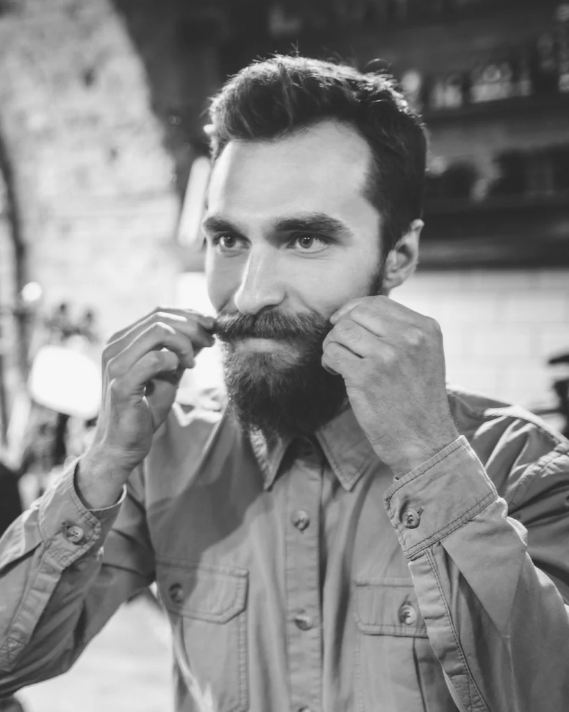 Man styling mustache wax through his mustache in the mirror for even hold and shape