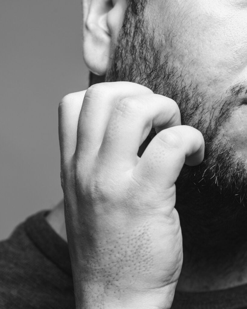 Man scratching an itchy beard, showing how irritation, rough handling and poor beard care can damage the beard you are trying to grow thicker.