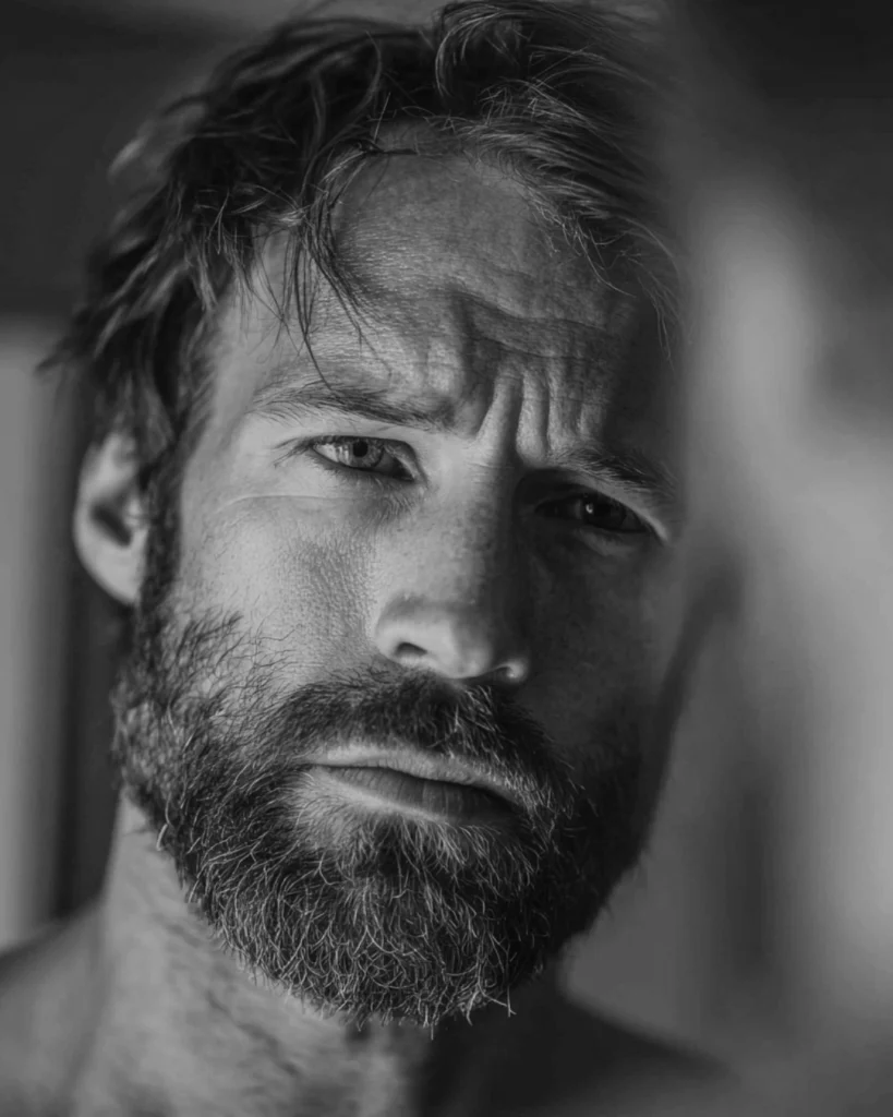 Man checking his beard in the mirror, showing why you should give beard growth enough time before judging patchy areas or trimming too early.