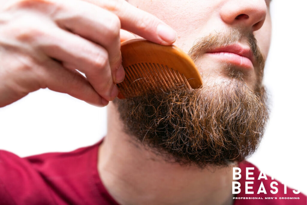 Close-up of a man combing his beard with a wooden comb, working to remove beard knots and maintain a smooth, well-groomed appearance.