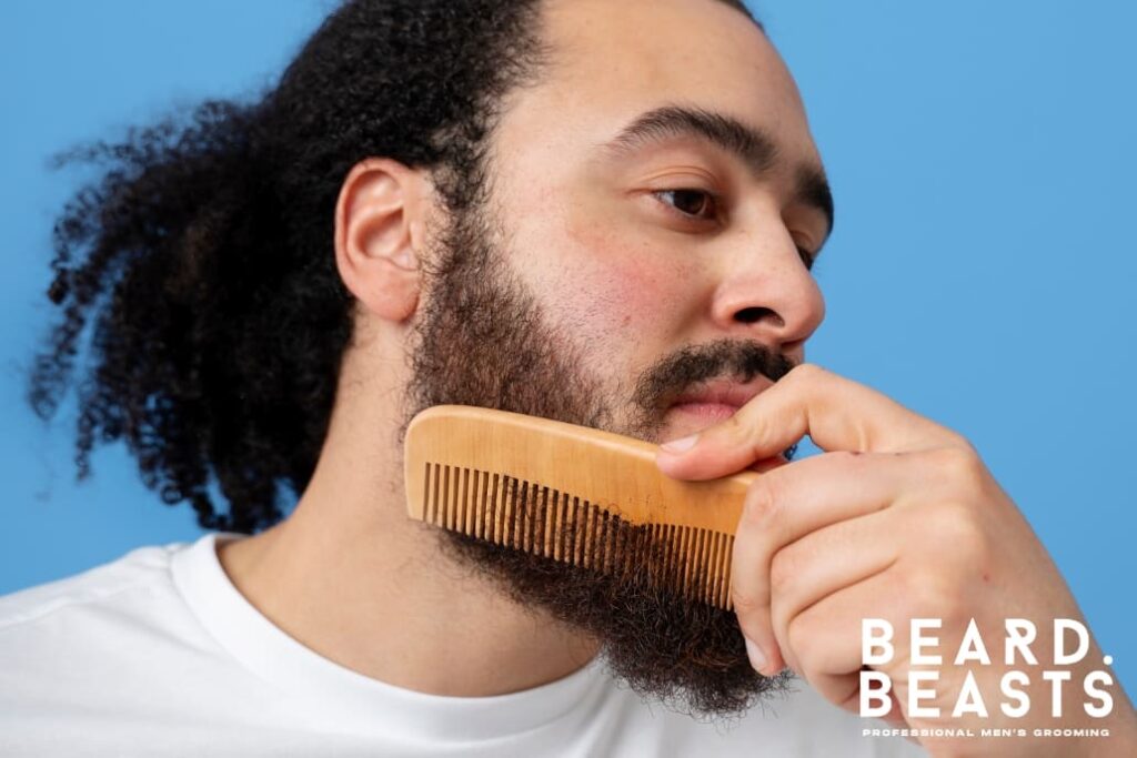 Man using a wooden comb to gently detangle his beard and remove beard knots, showcasing proper grooming techniques for maintaining a smooth and healthy beard.