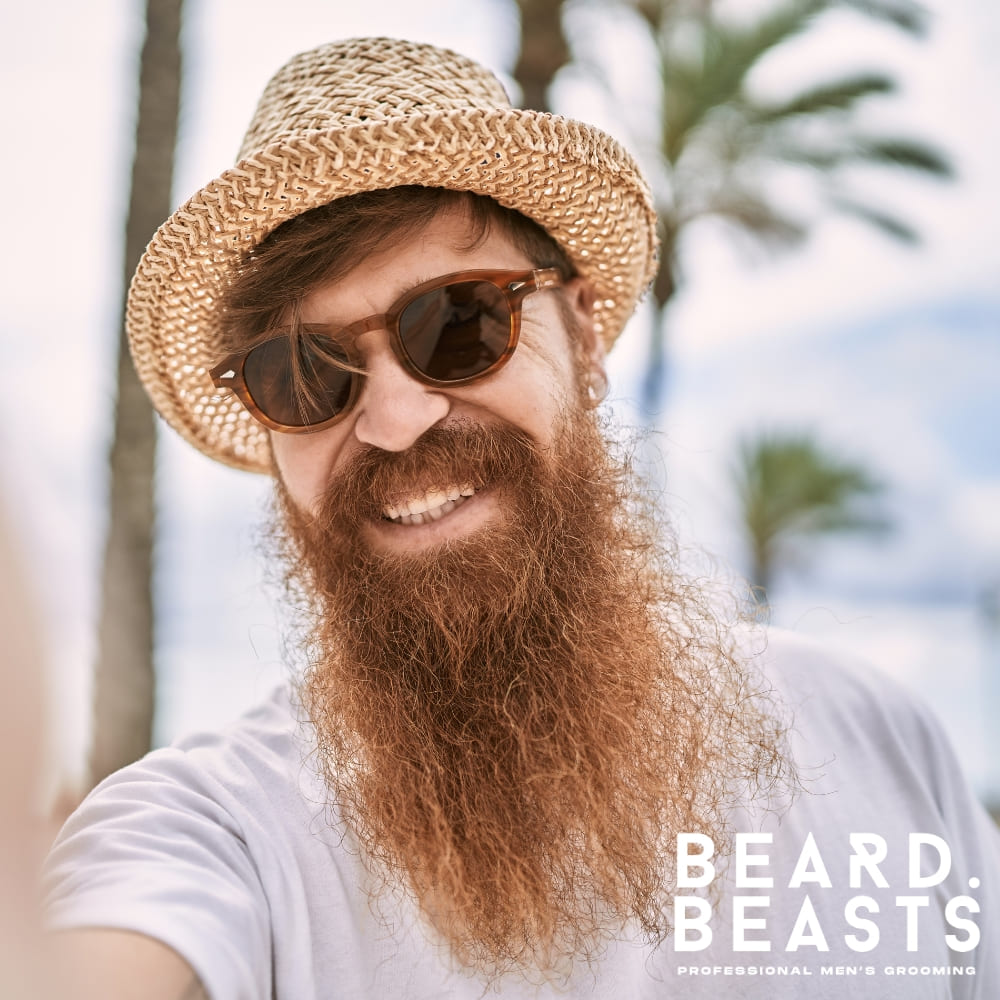 Close-up of a bearded man wearing an orange jacket, showcasing a thick, textured beard with shades of red, brown, and blonde. The Beard Beasts logo is visible, highlighting professional men's grooming expertise. Perfect for content exploring the topic, Why Is My Beard Turning Red?