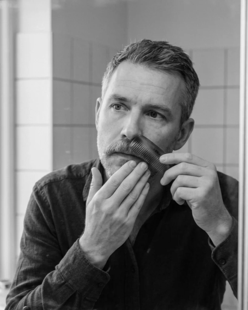Man combing a clean, dry mustache in the mirror before applying mustache wax