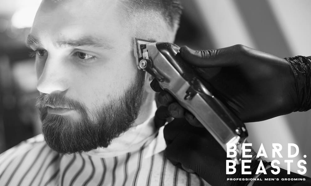 Barber trimming hair and beard in a professional barbershop, demonstrating grooming and haircut maintenance.