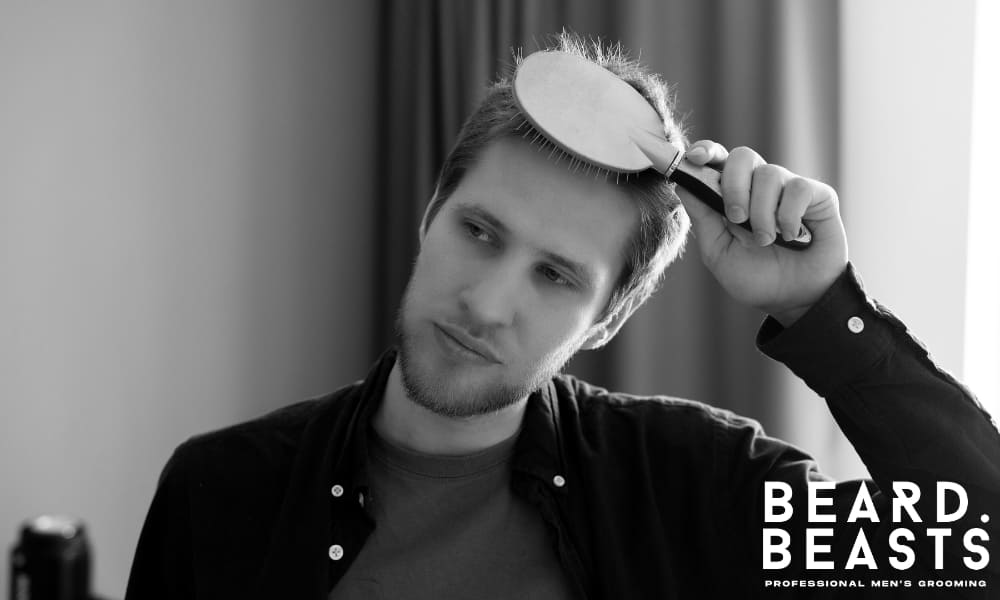 Man combing his damp hair to one side with a focused expression, showing clean grooming technique and product prep before styling.