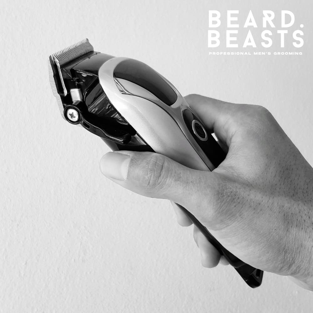 A close-up, black-and-white image of a hand holding a professional-grade hair clipper. The clipper features a sleek, modern design with metallic accents, emphasizing precision and quality. The neutral background keeps the focus on the tool, highlighting its role in achieving sharp and clean haircuts.