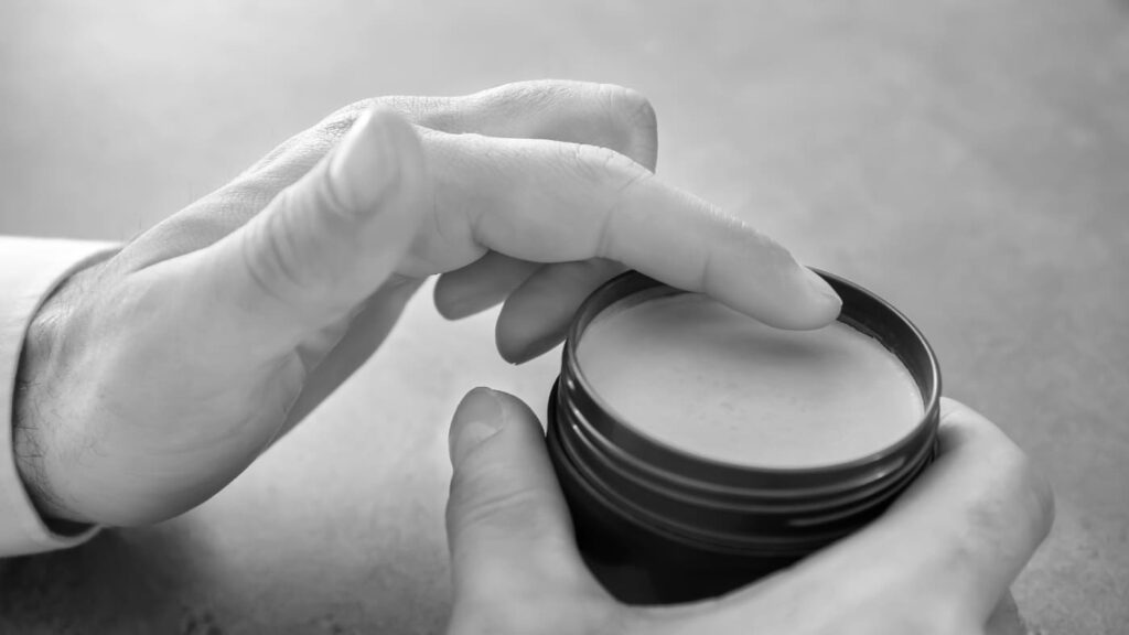 Close-up of a man scooping hair clay from a jar before styling