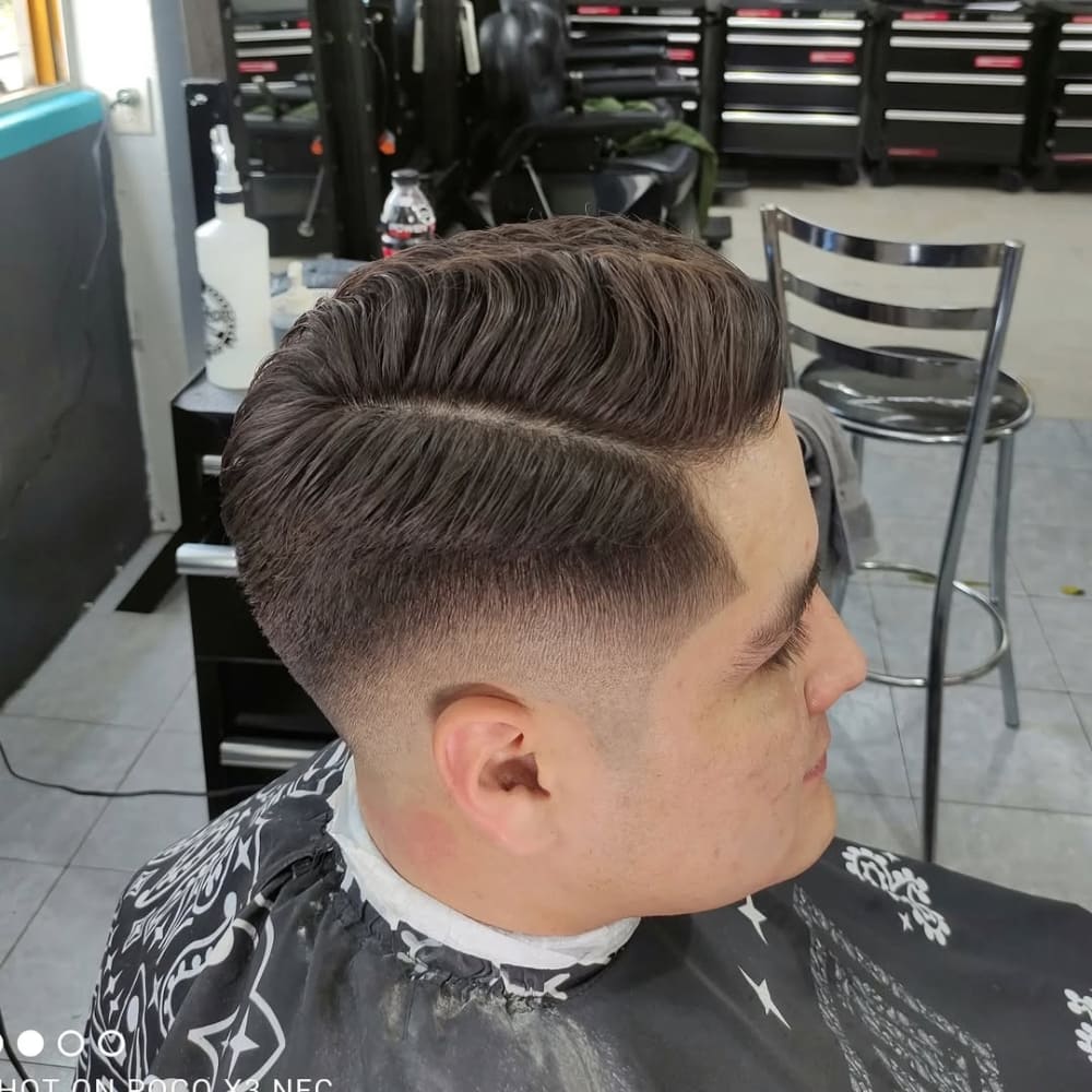 A man with a well-groomed mid fade comb over hairstyle, featuring a sharp, defined hard part and a clean fade on the sides, styled in a barbershop.
