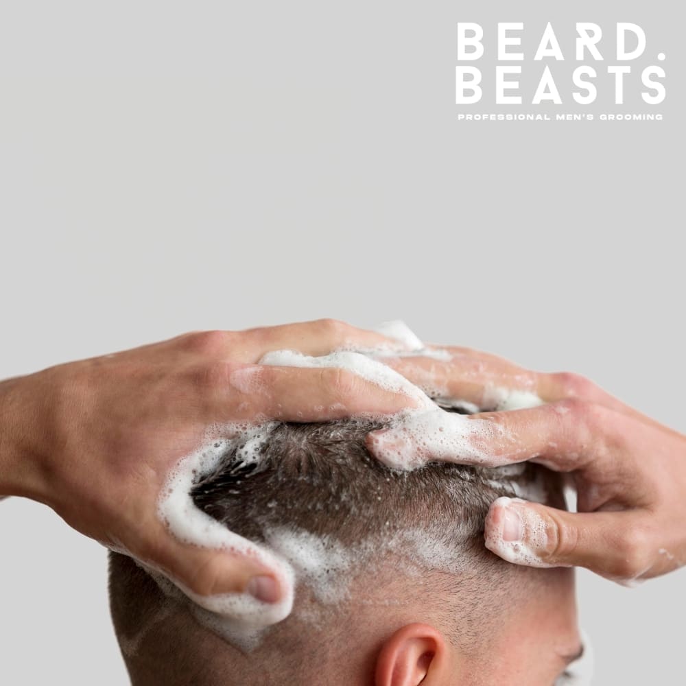 A close-up image of a man washing his hair, with hands lathering shampoo into short, neatly trimmed hair. The foam creates a clean, refreshing appearance, emphasizing proper hair care and hygiene. The light gray background keeps the focus on the grooming process, highlighting the importance of maintaining a healthy scalp. The "Beard Beasts – Professional Men's Grooming" branding in the corner underscores the professional and high-quality approach to men's grooming.