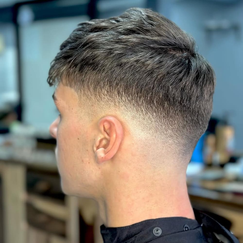 A man with a clean and stylish mid fade haircut, featuring a gradual blend from longer hair on top to shorter sides, showcasing a natural and polished look. The haircut transitions smoothly without exposing the skin, ideal for both casual and professional settings.