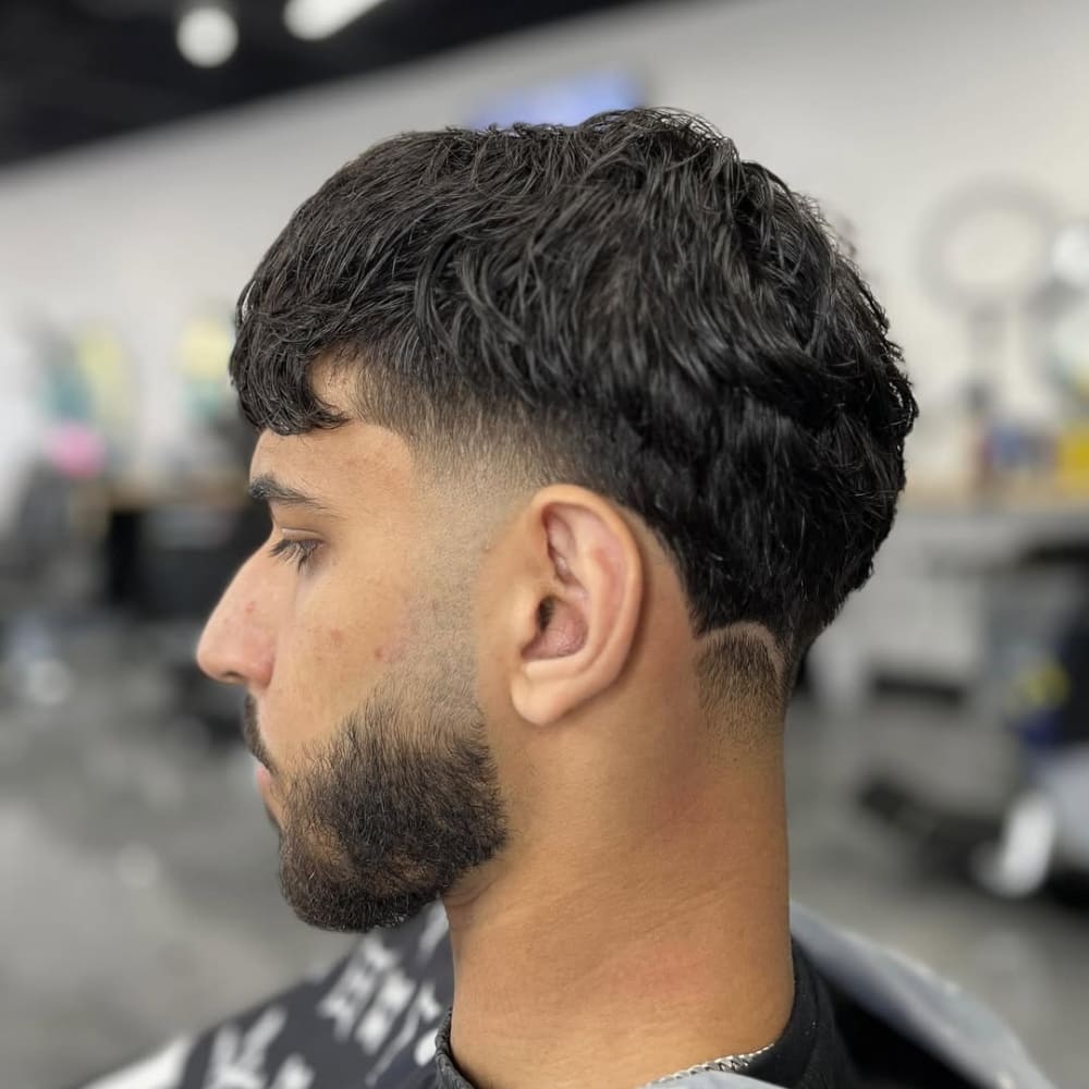 A side profile of a man with a clean mid taper haircut, featuring a gradual fade starting above the ears, complemented by a well-groomed beard.