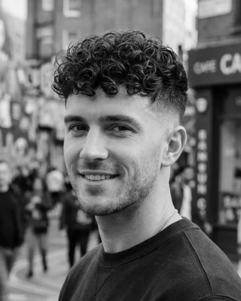 Man with curly hair and a mid skin fade, showing how a curly top works with faded sides and natural texture.