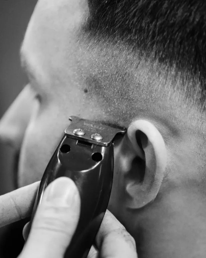 Barber trimming a mid skin fade around the ear, showing how regular barber work keeps a skin fade looking tight.