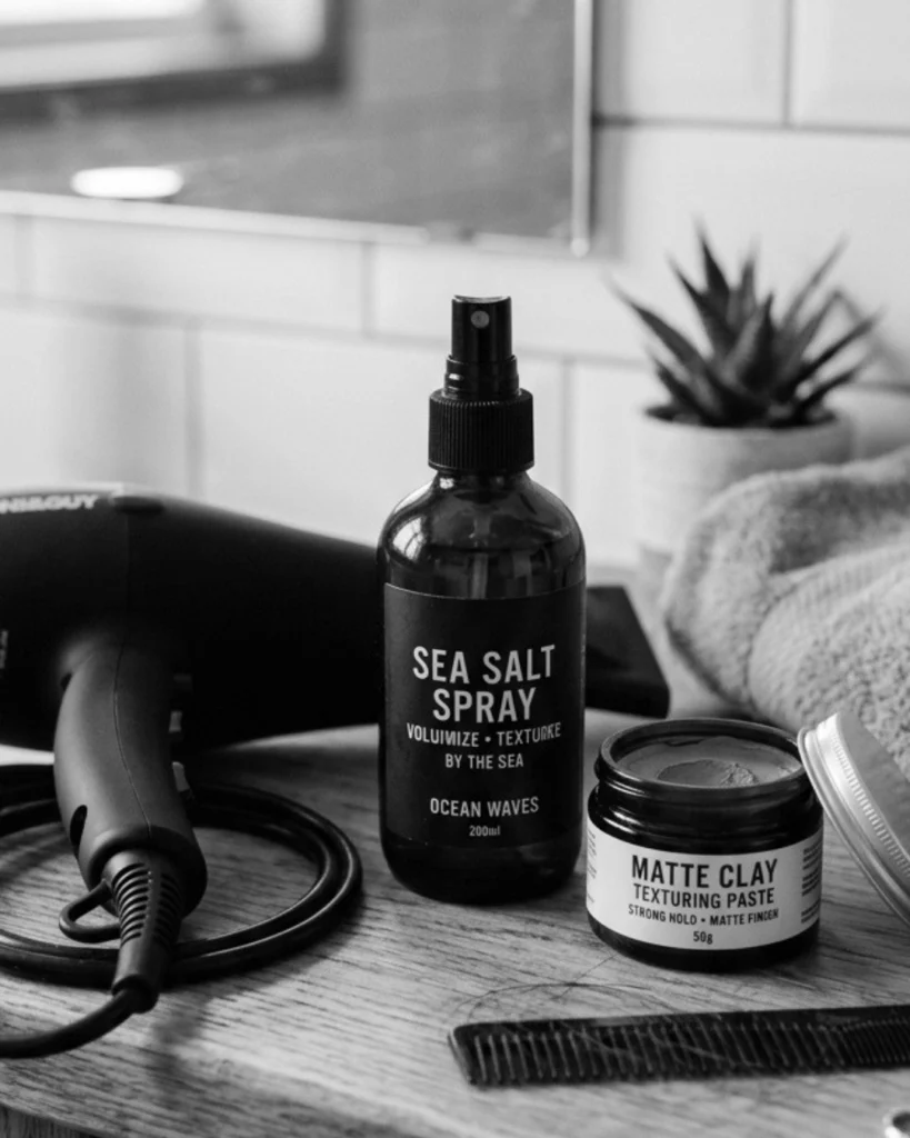 Sea salt spray beside a hair dryer and matte clay, showing how it works as a pre-styler before finishing the hairstyle.