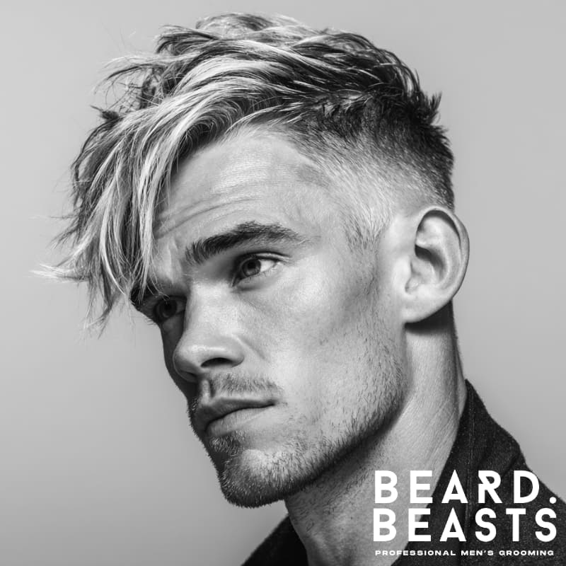 Side-swept high fade fringe hairstyle for men with blonde highlights, featuring a voluminous, tousled top and clean, sharp fade on the sides.