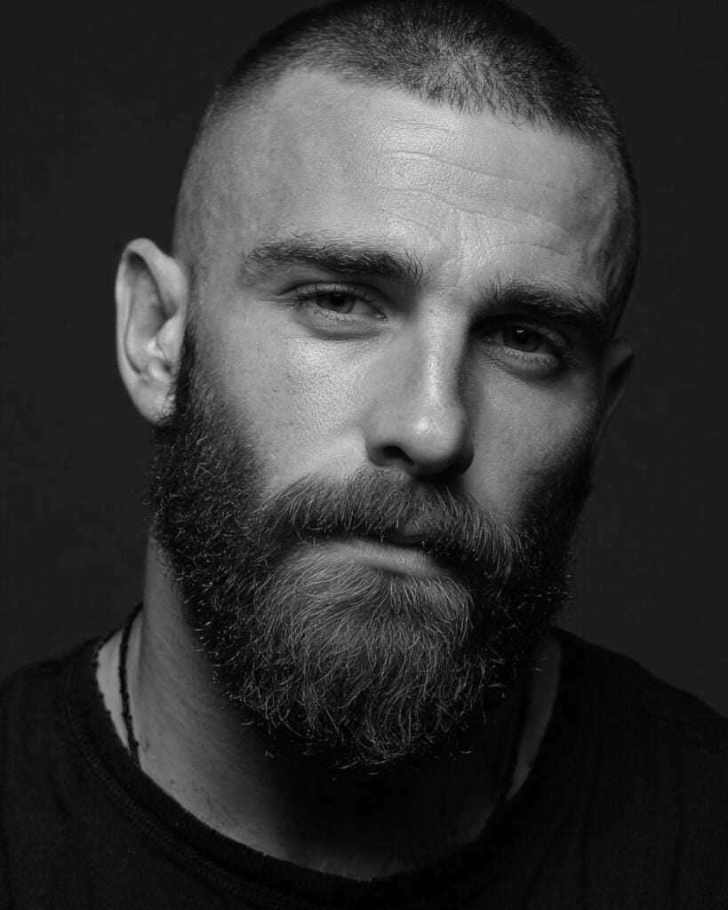 buzz cut and full faded beard combination on a man with dark hair, front view portrait