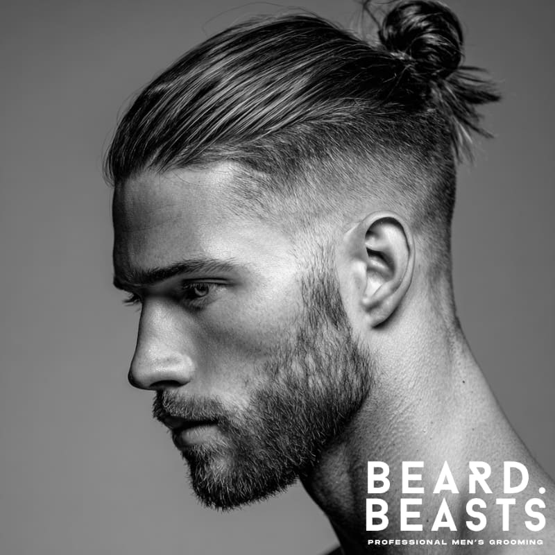 Side profile of a man with a high skin fade and straight hair tied into a neat man bun, paired with a light beard and defined jawline.