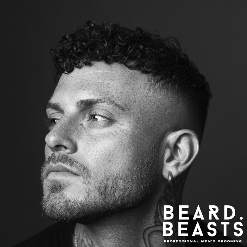 Side profile of a man with short curly hair on top and closely faded sides, looking slightly upward in a black and white portrait.