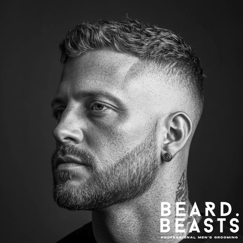 Side profile of a man with short hair on top and a clean skin fade, featuring defined edges, a trimmed beard, and a visible neck tattoo.