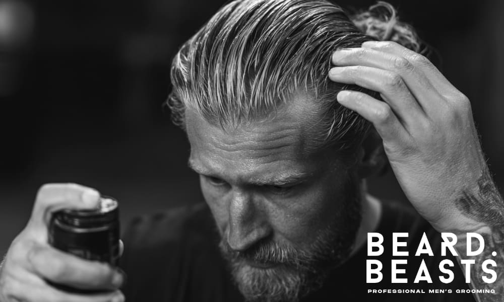Man styling his hair by warming product between his hands, with slicked-back hair and focused expression during grooming routine.