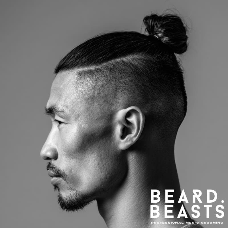 Side profile of a man with straight hair in a high, tight man bun and a disconnected high fade, featuring a sharp jawline and minimal facial hair.