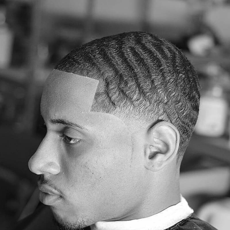 Close-up of a man with defined 360 waves and a low taper fade, sitting in a barbershop.