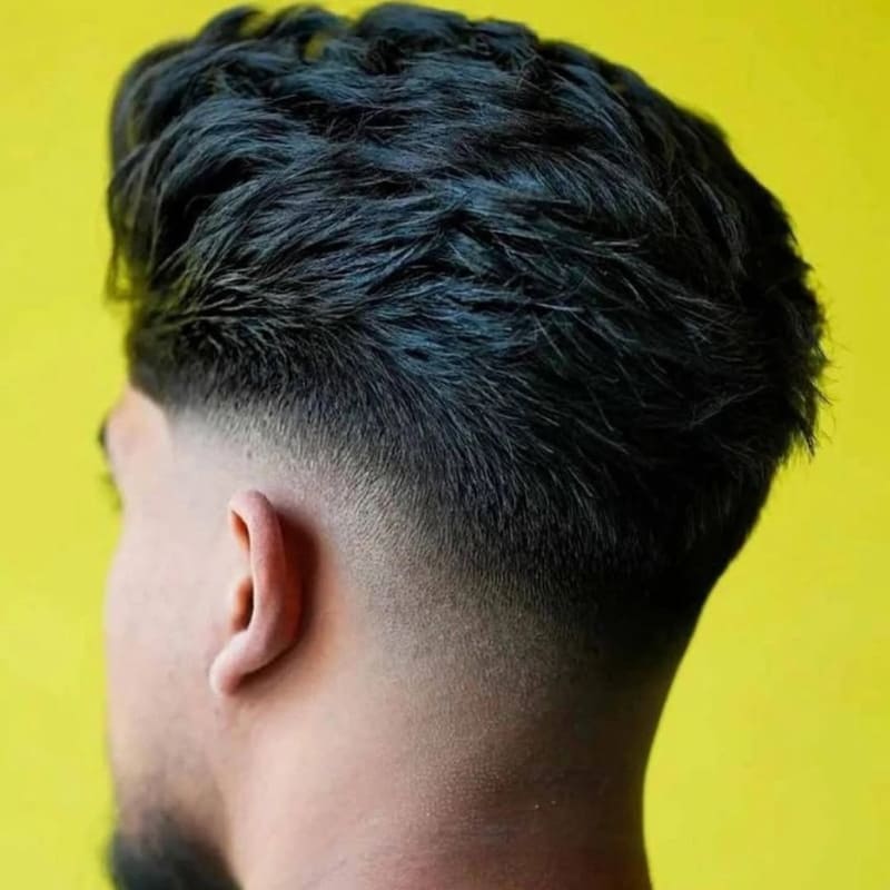 Back view of a low fade textured slick back hairstyle on thick black hair, showcasing clean tapering and natural volume on top against a yellow background.