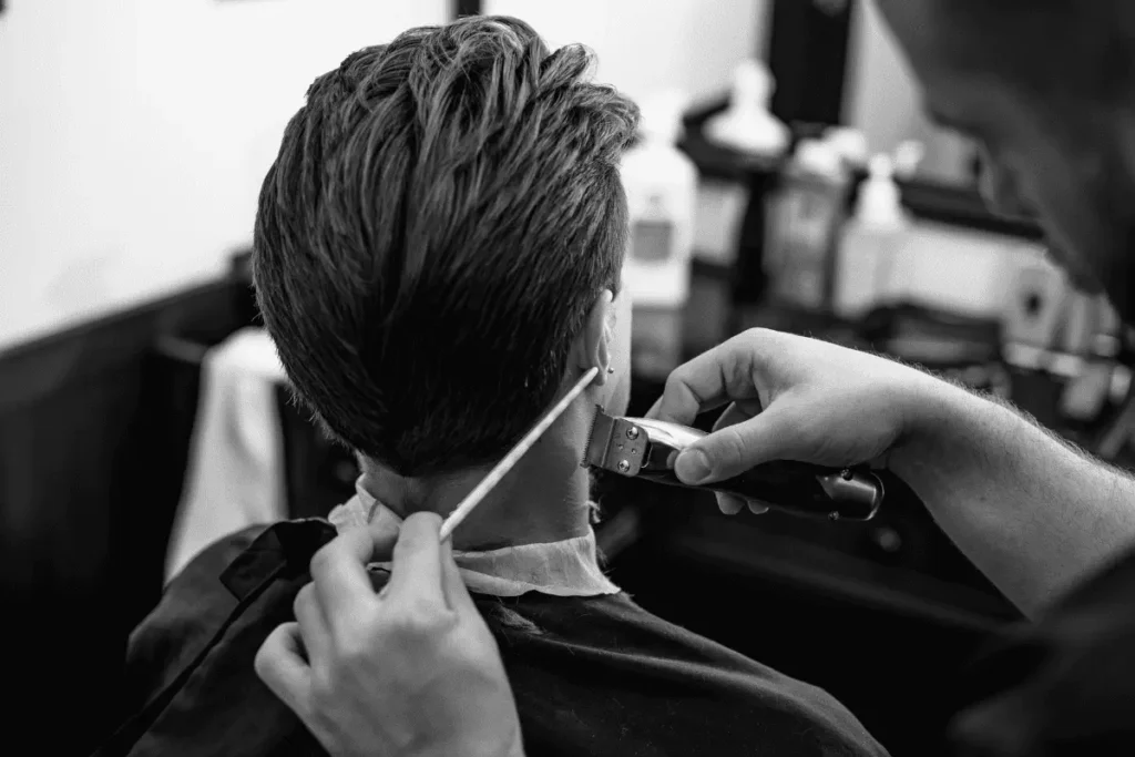 Barber trimming the back and neckline of a textured slick back haircut on a man in a barbershop