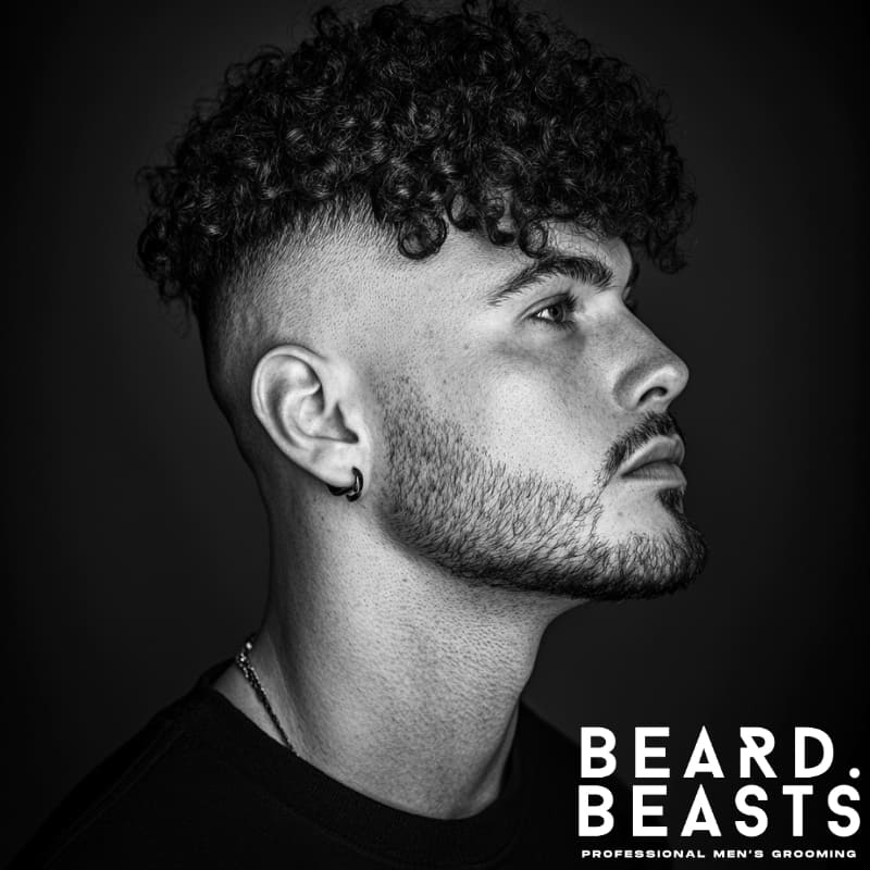 Side profile of a man with a sharp curly undercut featuring dense, coiled curls and a clean skin fade.