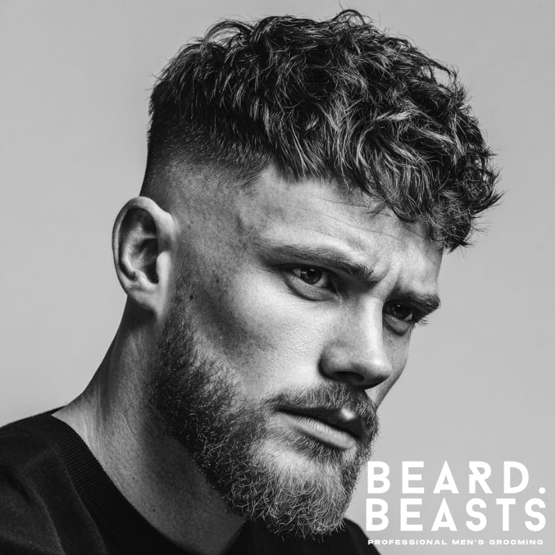 High fade textured fringe haircut with voluminous curls on top and a clean fade on the sides. Modern, bold style perfect for a sharp and stylish look.