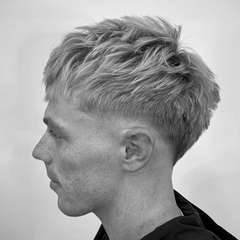 Low fade haircut with textured hair on top, styled with soft layers for a natural, voluminous look. A clean and modern style offering a fresh, minimalistic appearance.