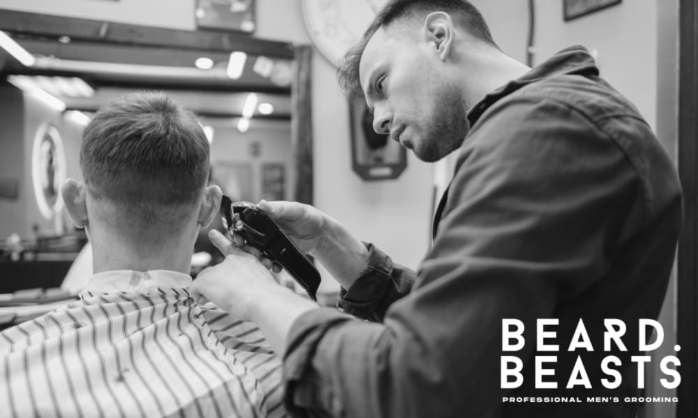 Black and white photo of a barber giving a client a precise cut using clippers, with Beard Beasts professional grooming logo in the corner.
