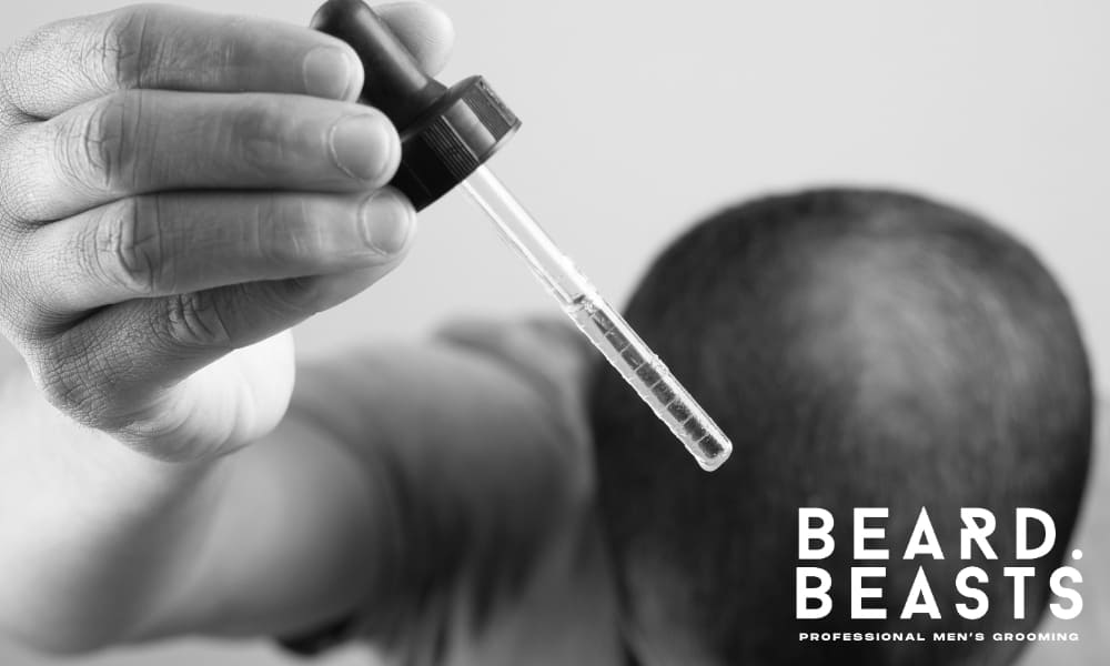 Man applying topical minoxidil with dropper to scalp for hair regrowth treatment, addressing male pattern baldness – Beard Beasts professional men’s grooming solution for hair loss.