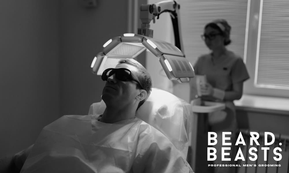 Man undergoing red light laser therapy for hair loss treatment in a professional clinic, wearing protective glasses under LED device – Beard Beasts professional men’s grooming and hair restoration solution.
