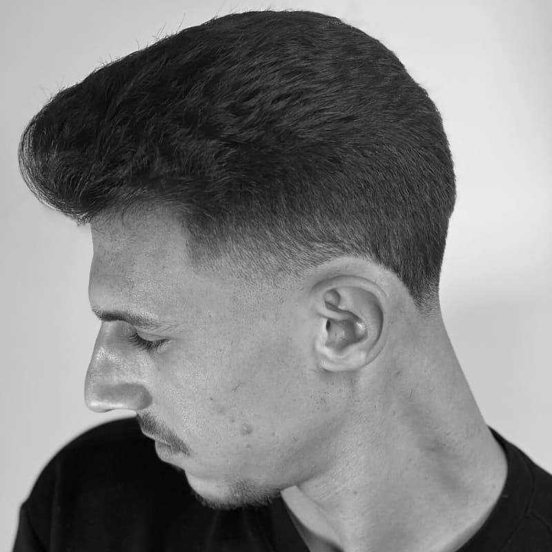 Man with a short pompadour haircut and faded sides, looking down in a studio setting.