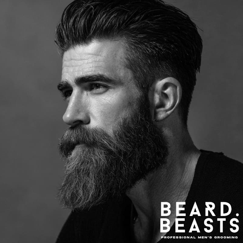Textured slick back hairstyle with a full beard for men, featuring voluminous top and clean faded sides.