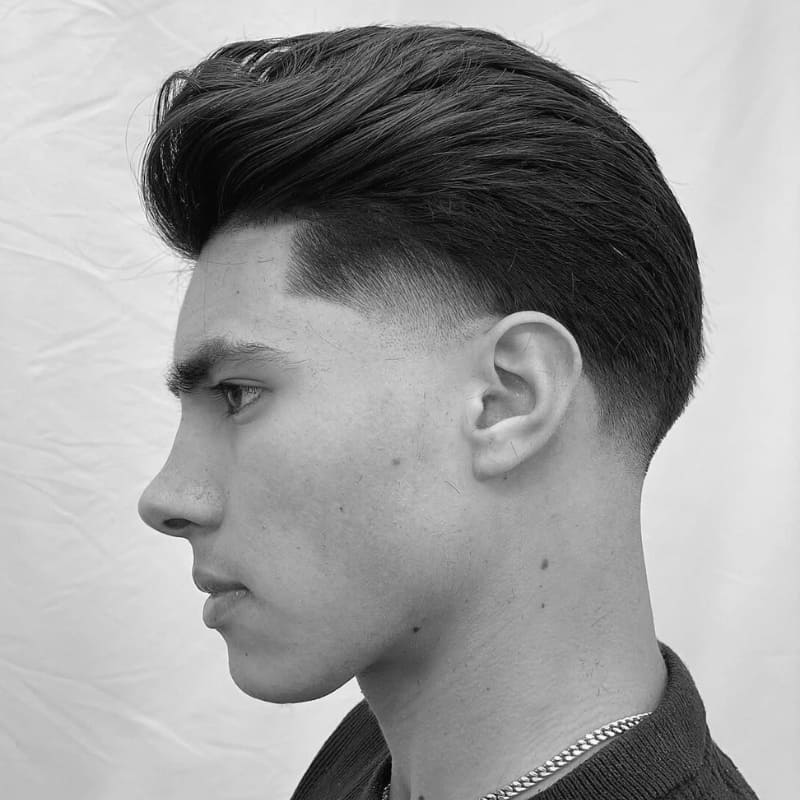 Textured slick back hairstyle with taper fade, featuring voluminous top and clean, blended sides for a modern, sharp look.