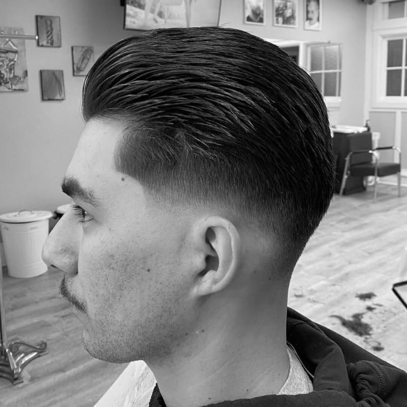 Man with a neatly styled slicked back haircut featuring textured volume on top and a clean low fade on the sides, photographed in a barbershop setting.