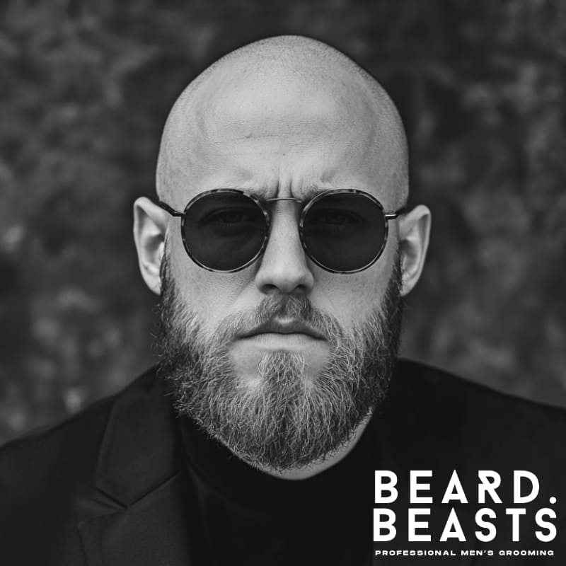 Stylish bald man with a short, well-groomed beard and sunglasses—showcasing a modern beard style for bald guys.