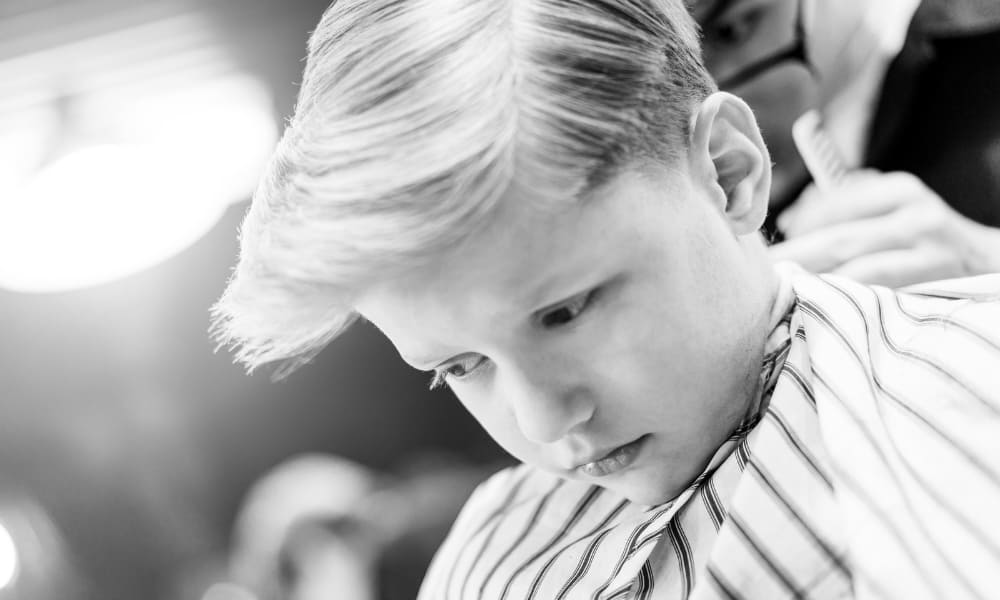 Young boy getting a stylish haircut for thick hair at a barbershop—classic choice among the best haircuts for kids with thick hair.