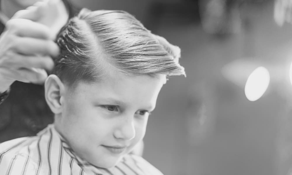 Barber styling a classic side part haircut for a boy with thick hair—one of the best haircuts for kids with thick hair that’s clean and timeless.