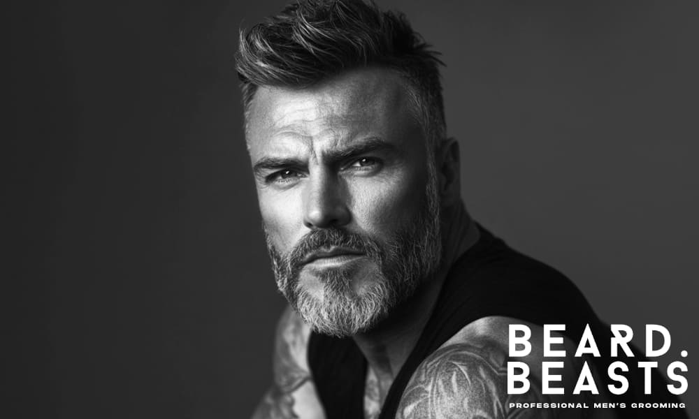 Black and white portrait of a confident, well-groomed man with a styled haircut and beard, symbolizing precision and timeless masculine style.