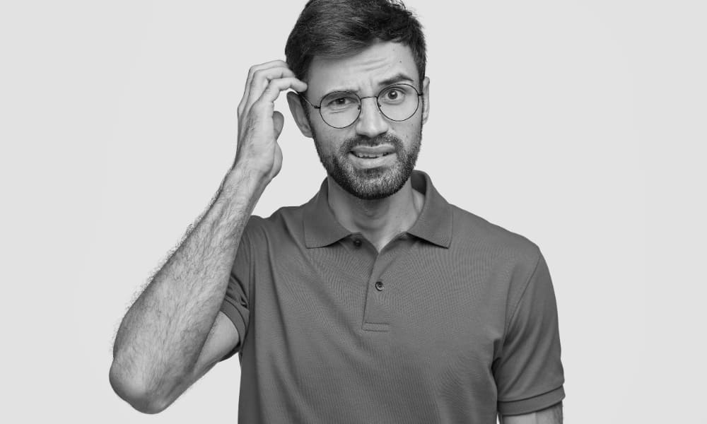 Confused man with short facial hair and glasses scratching his head, looking for answers.