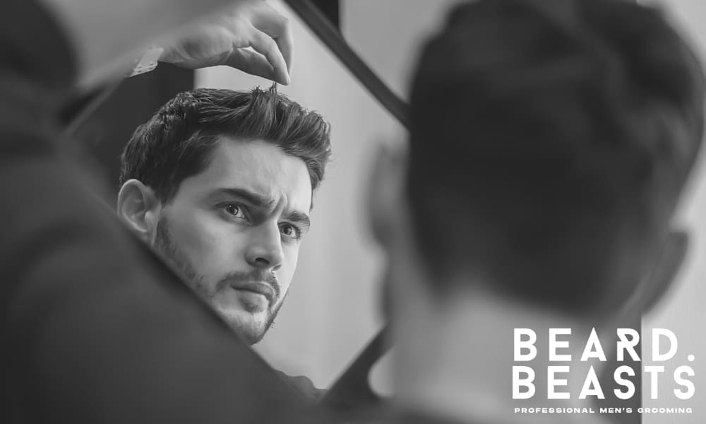 Man styling hair in front of mirror as part of a daily routine to prevent flat hair in men.
